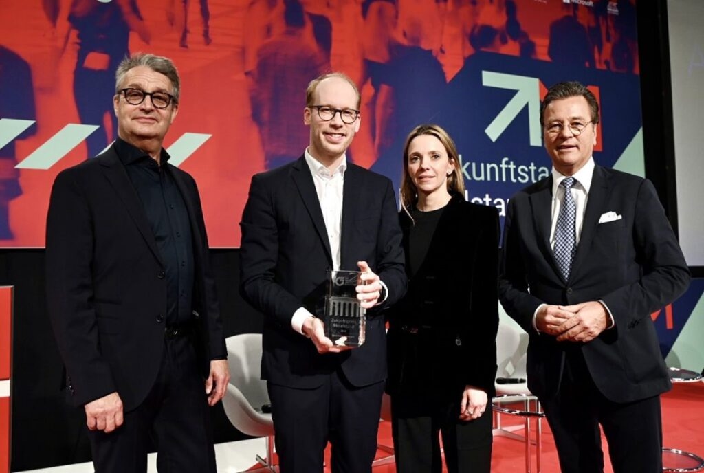 A photo of group of four people looking at a camera with one person holding an award